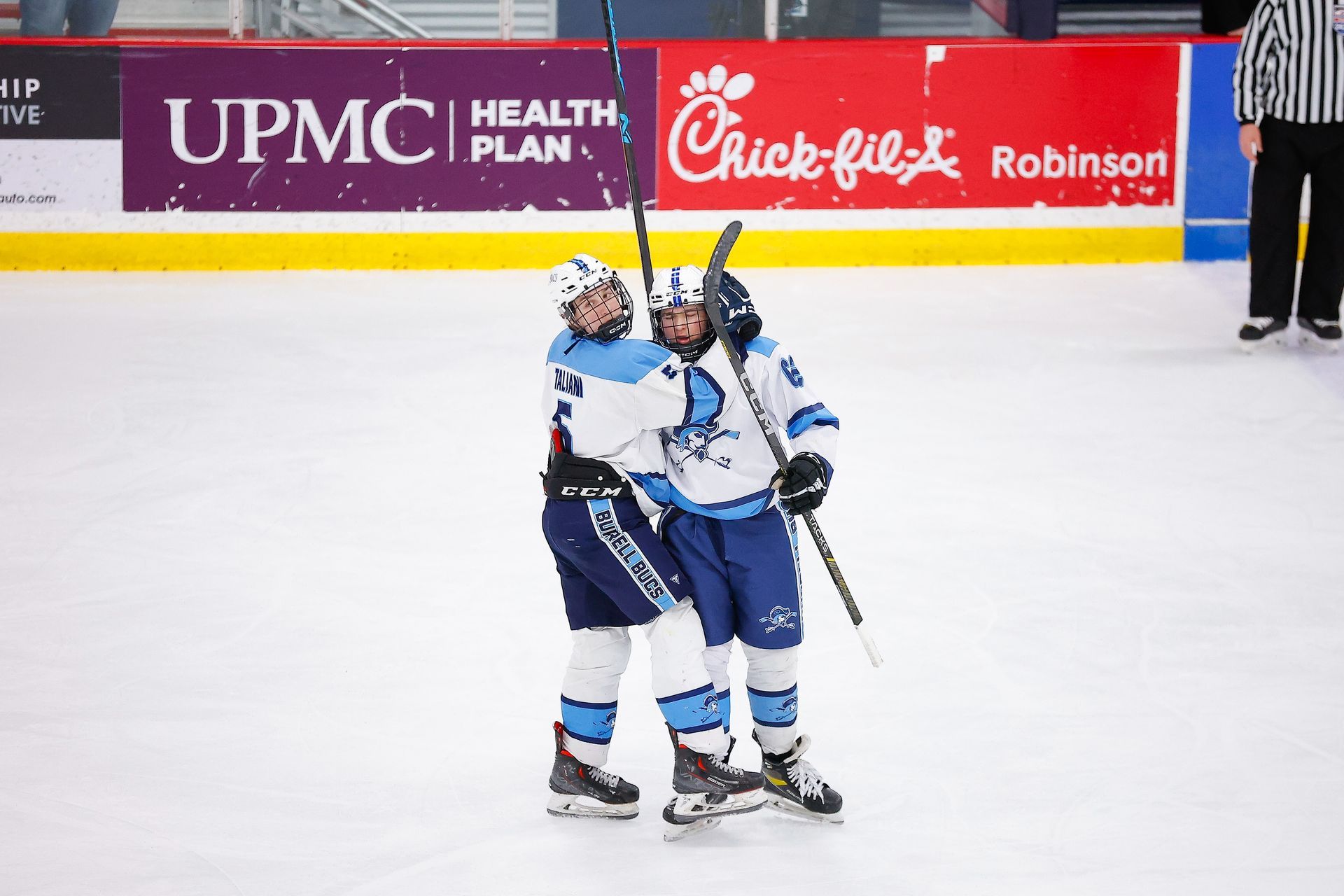 Two hockey players in white and blue uniforms embrace on the ice in celebration.