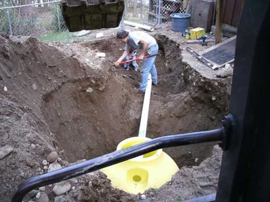Worker digging a trench around a yellow pipe in a muddy construction site