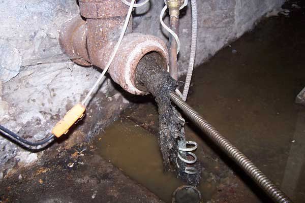 Rusty pipe draining dark water into a flooded basement floor