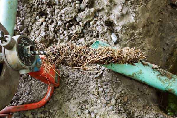 Damaged green pipe with exposed frayed cable and red conduit in muddy ground