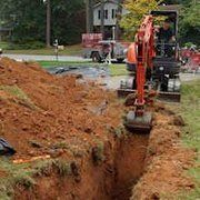 Orange excavator digging a trench beside a dirt pile on a residential street