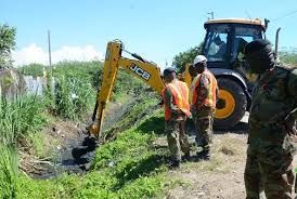 Workers digging a ditch beside a yellow backhoe in a grassy rural area