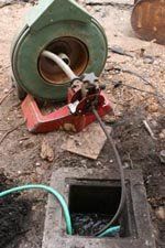 Green reel on red stand feeding hose into a square ground opening outdoors