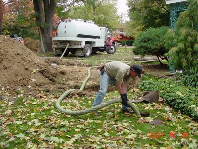Worker using a hose to clean leaves in a garden beside a white tank truck