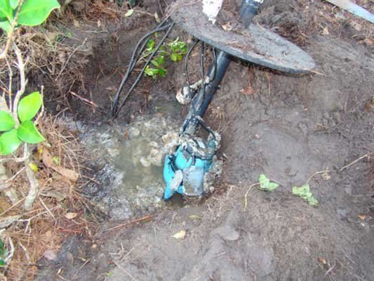 Blue utility valve in a muddy dirt hole with water pooling around it