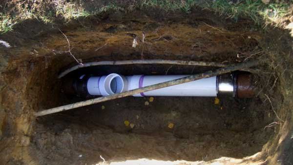PVC pipe and white cable laid in a narrow underground trench with exposed dirt walls