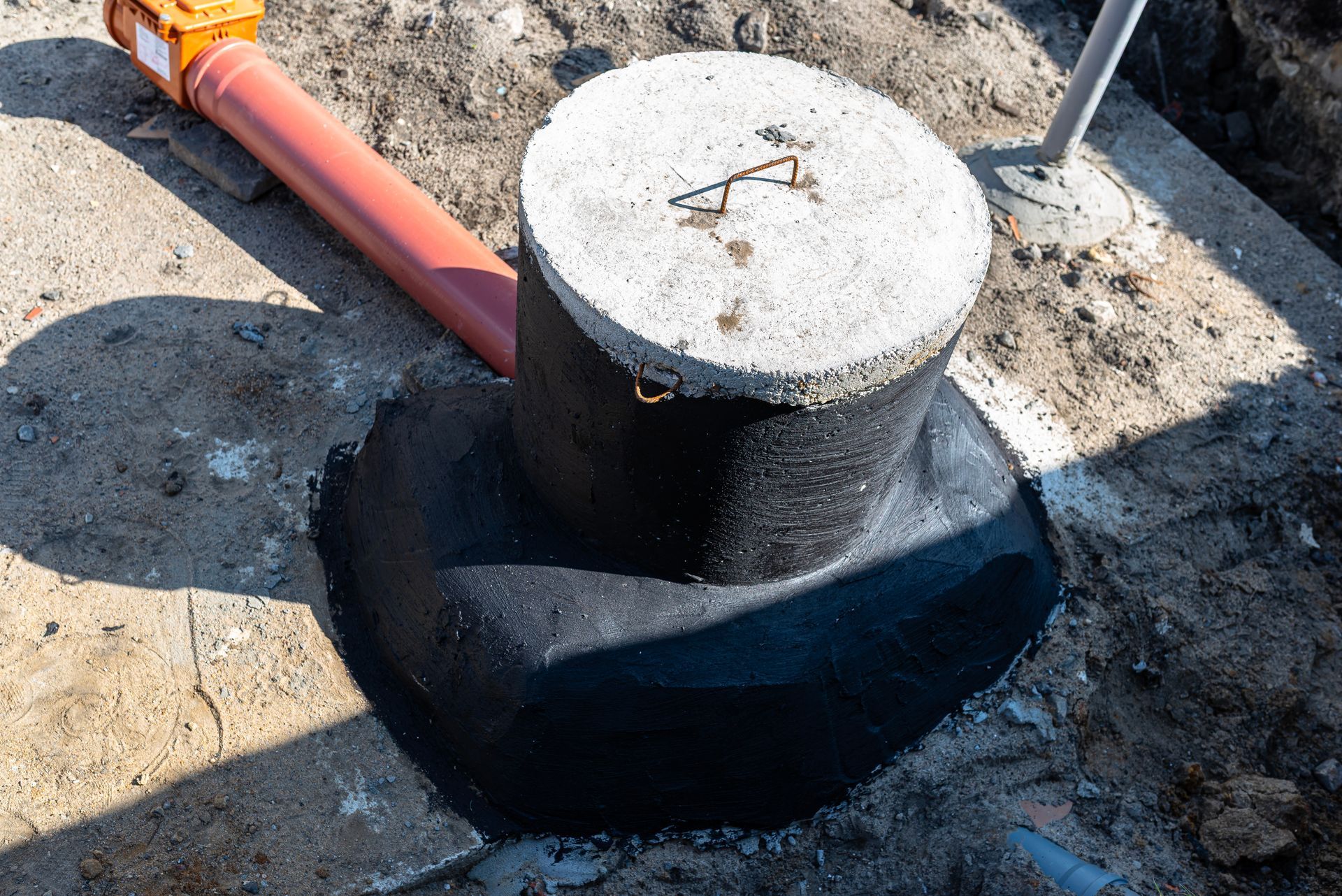 Concrete utility box and orange conduit installed in a dug trench outdoors