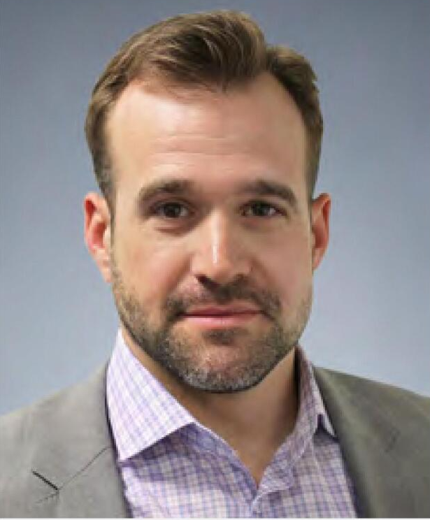 A man with a beard is wearing a suit and a purple plaid shirt.