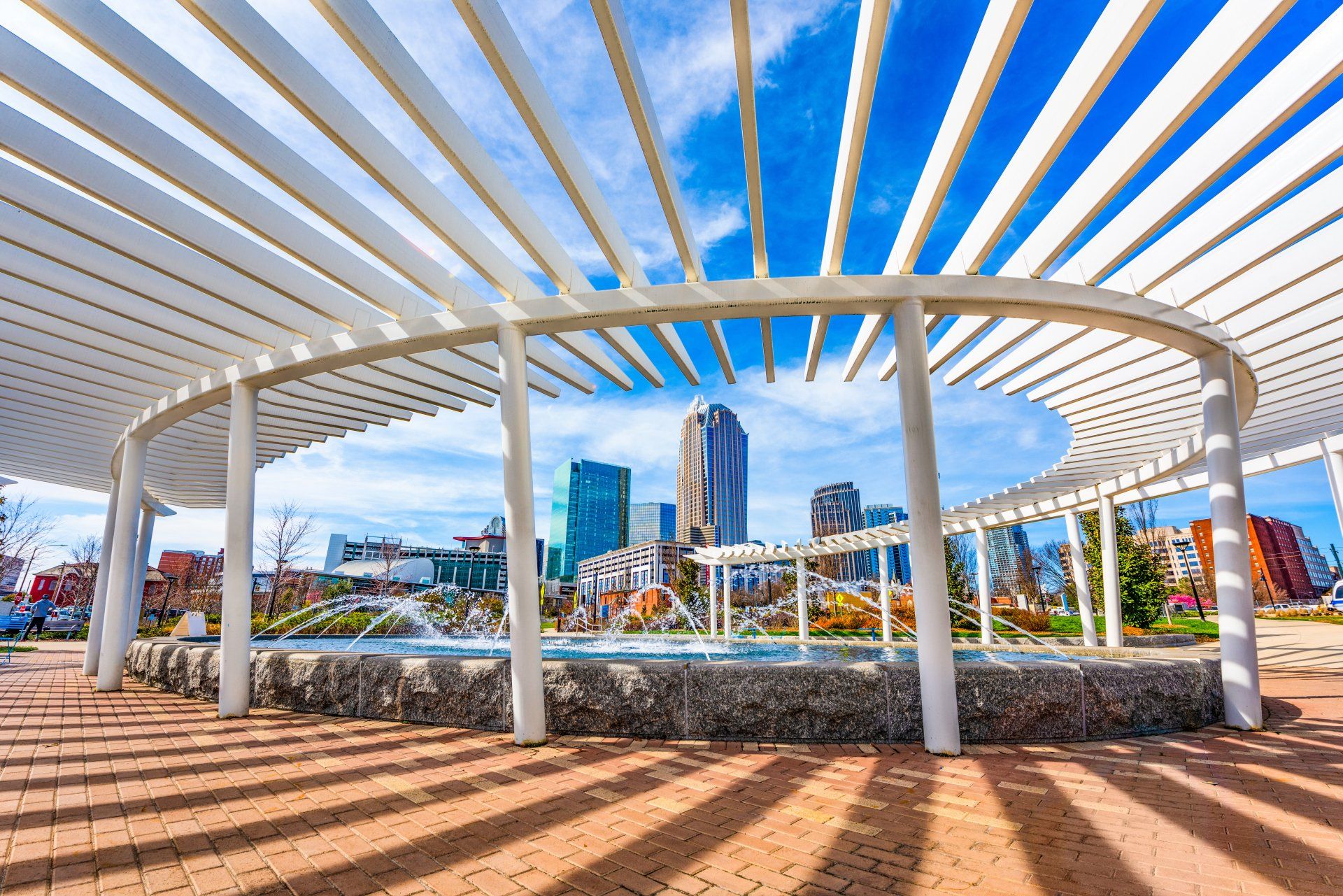 There is a fountain in the middle of the park under a pergola.