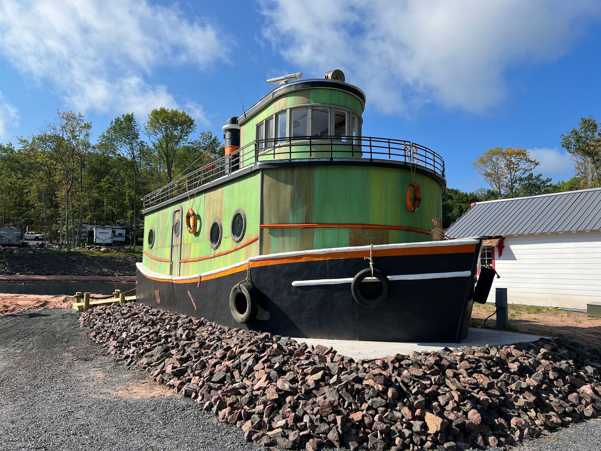 Green and black boat-shaped building on a stone foundation, under a blue sky.