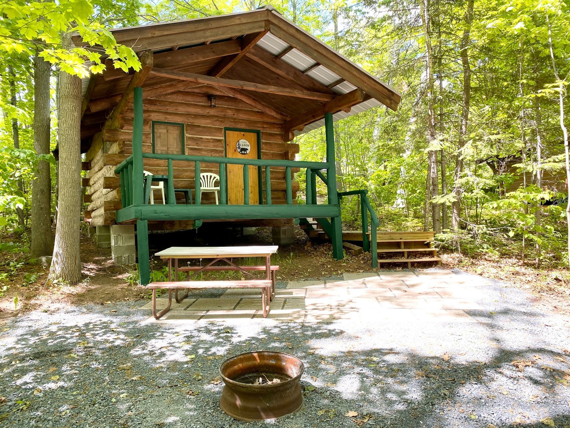 Cabin with green trim, picnic table, and fire pit in a wooded area.