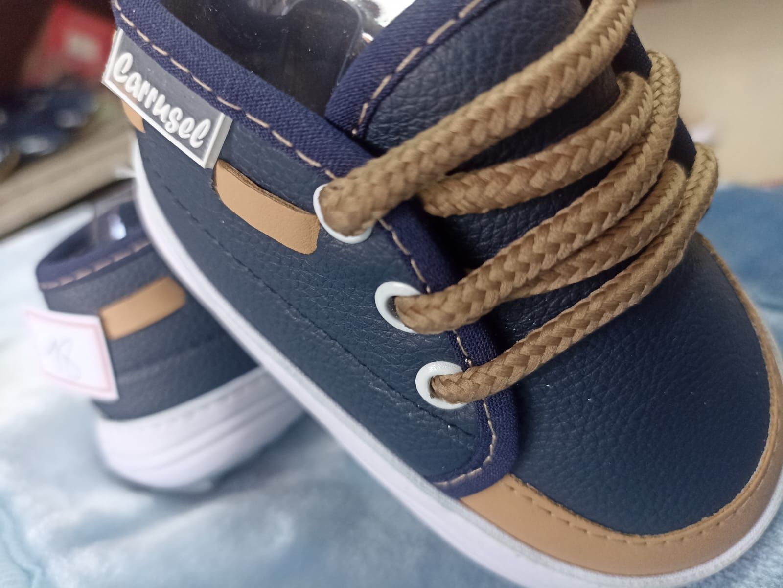 Zapatillas azules para bebé con detalles en color tostado y cordones gruesos sobre una manta suave.