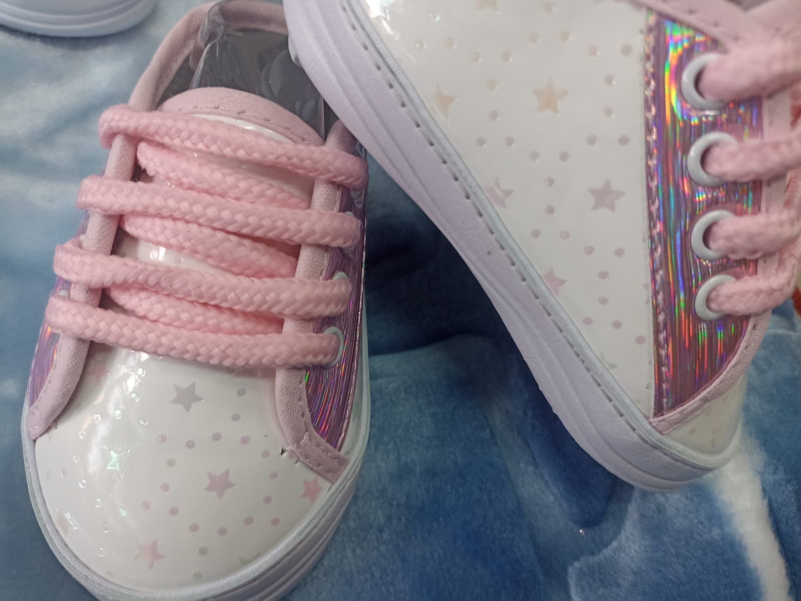 Zapatillas rosas con estampado de estrellas blancas y cordones, mostradas una al lado de la otra sobre tela vaquera.