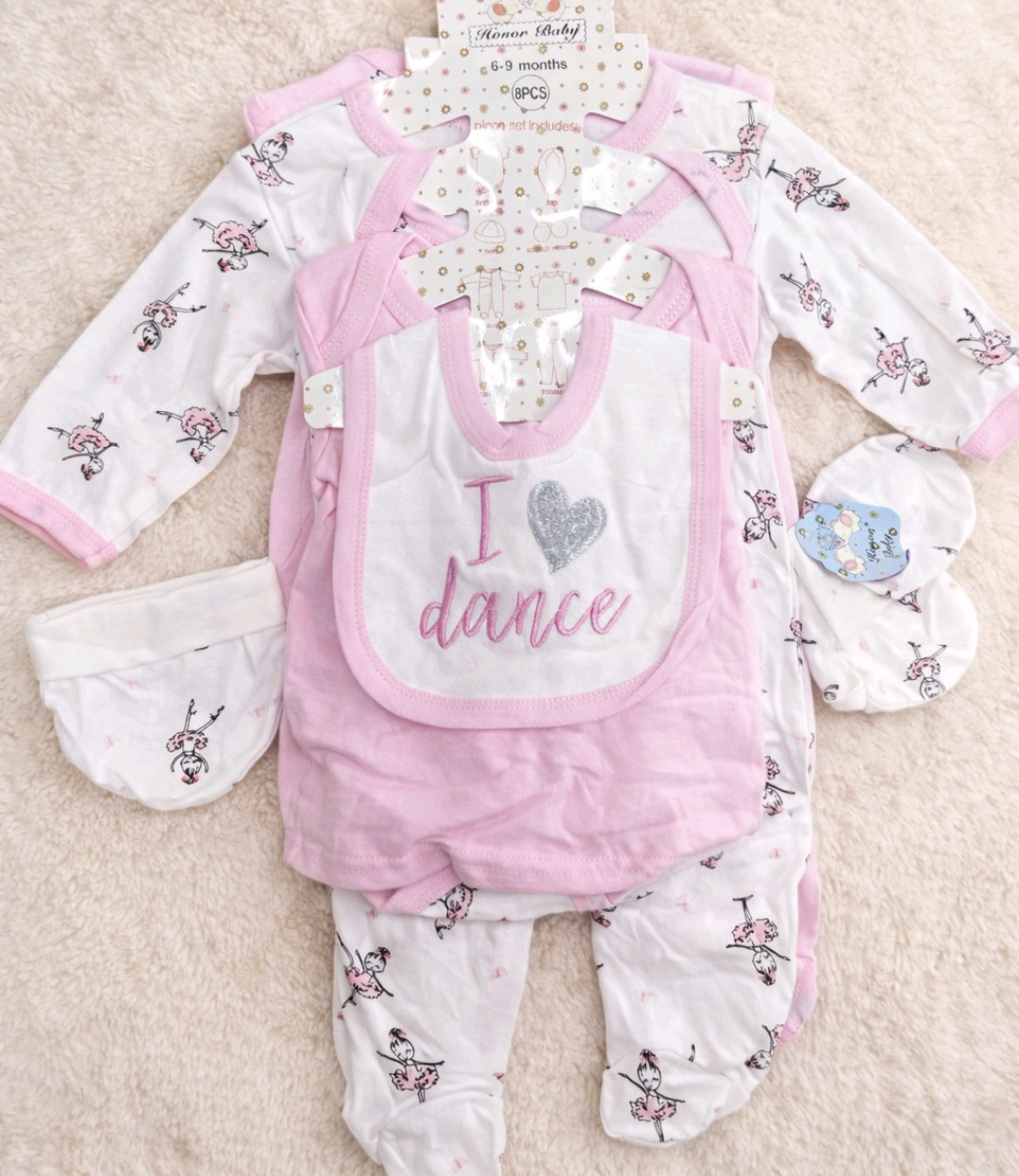 Conjunto de ropa para bebé que incluye un body floral rosa y blanco, un babero rosa, un gorro y manoplas a juego.