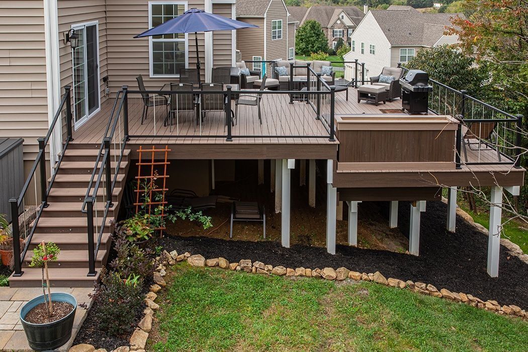 Backyard deck with stairs, patio furniture, grill, and blue umbrella over a raised wooden platform