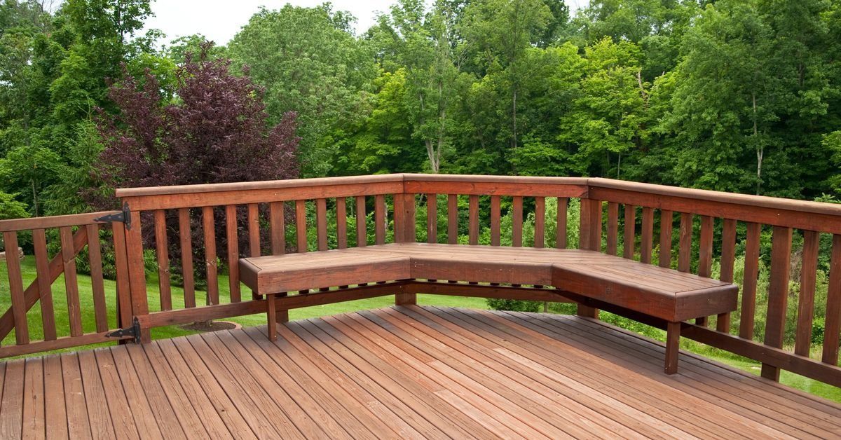 Wooden deck with curved bench seating overlooking a lush green backyard garden.