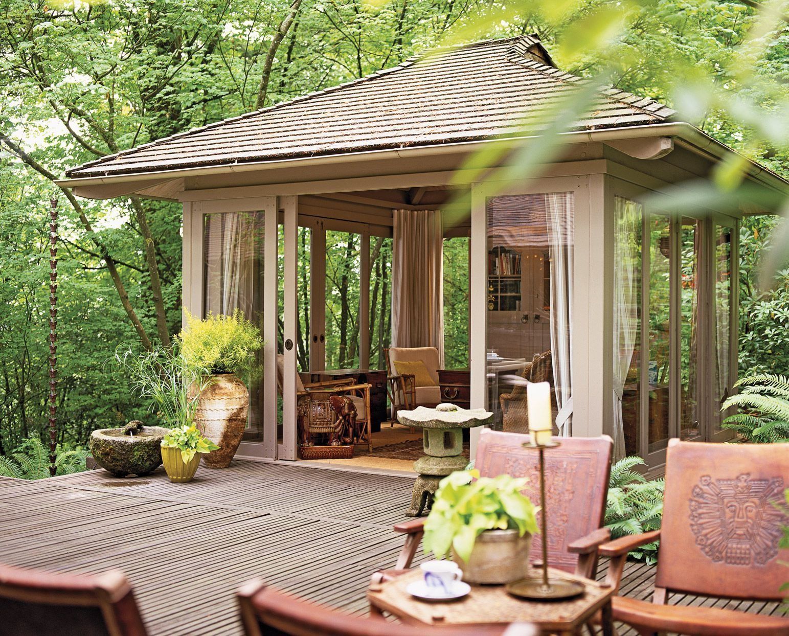 Cozy outdoor patio with wicker chairs, pink cushions, potted plants, and a gazebo in a lush green garden.