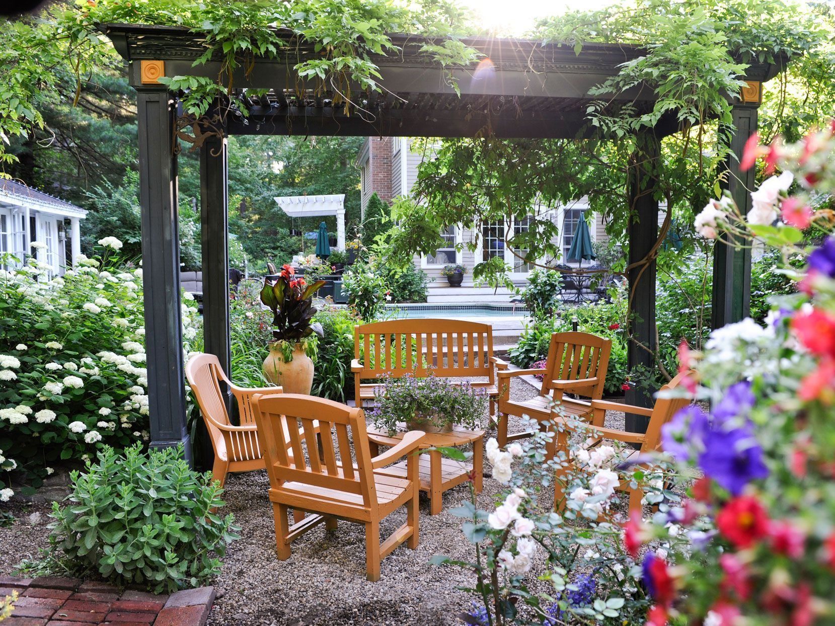 Wooden garden seating under a leafy arbor, surrounded by colorful flowers and greenery