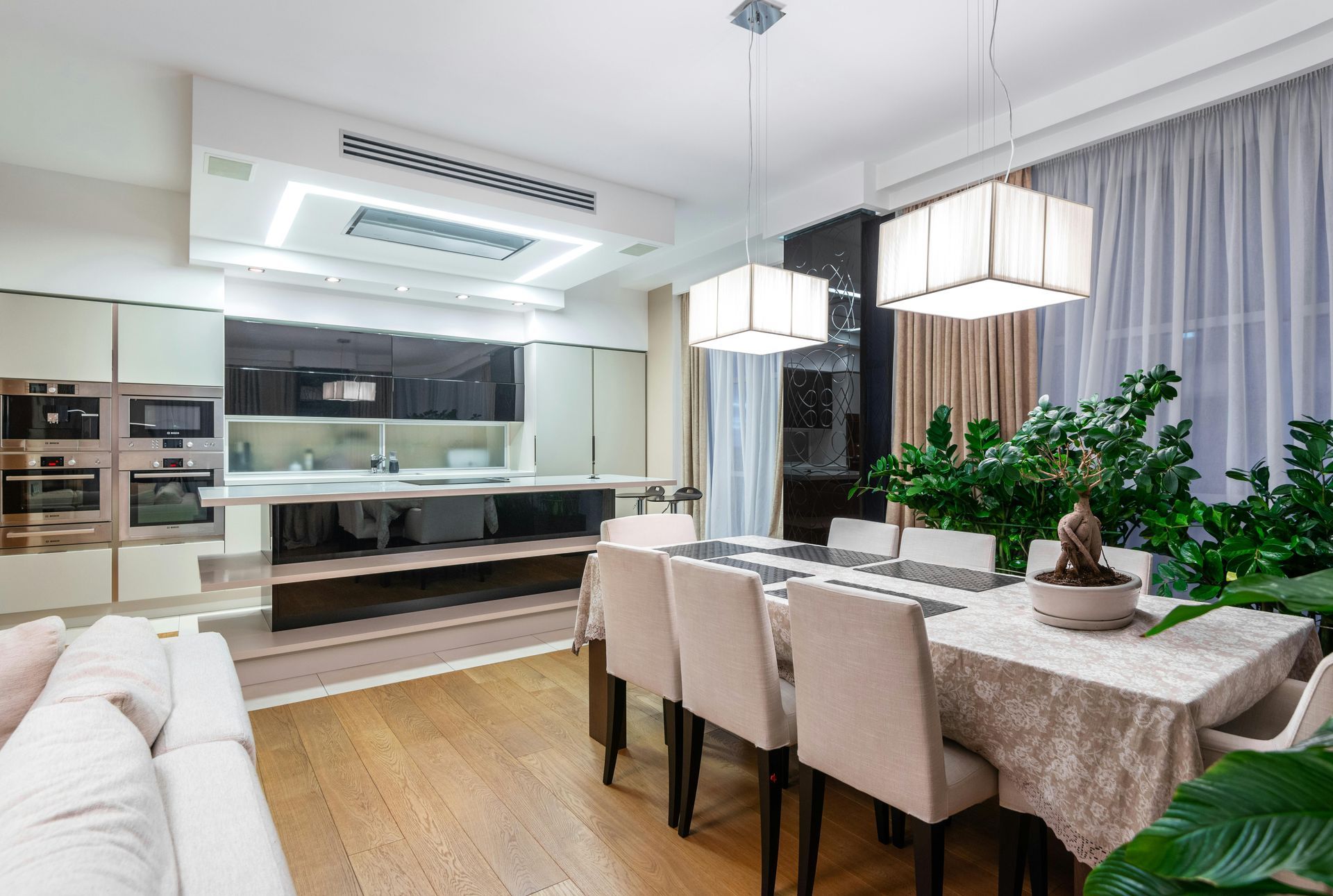 Modern open-concept dining room with a set table, white sofa, and sleek kitchen in the background