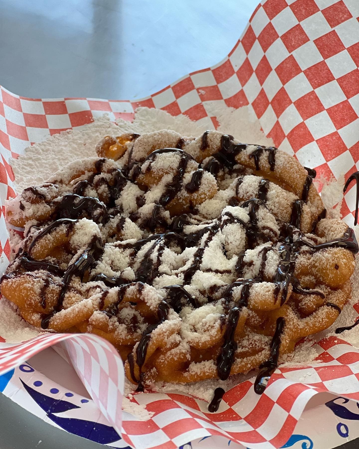 Powdered pastry with chocolate drizzle in red-and-white checkered paper basket