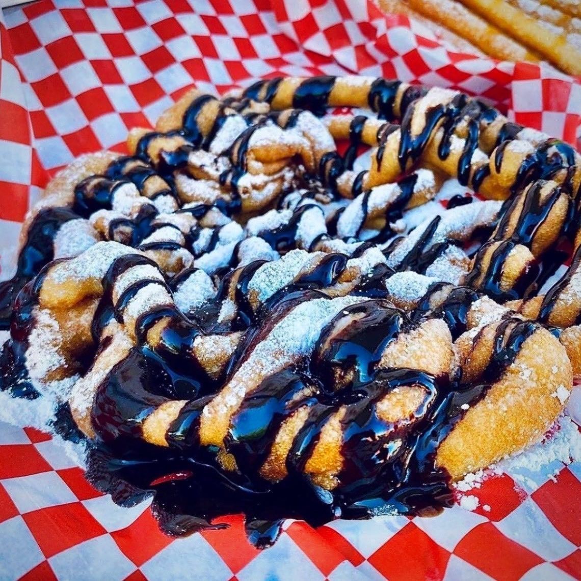A pastry drizzled with chocolate and powdered sugar on red-and-white checkered paper.