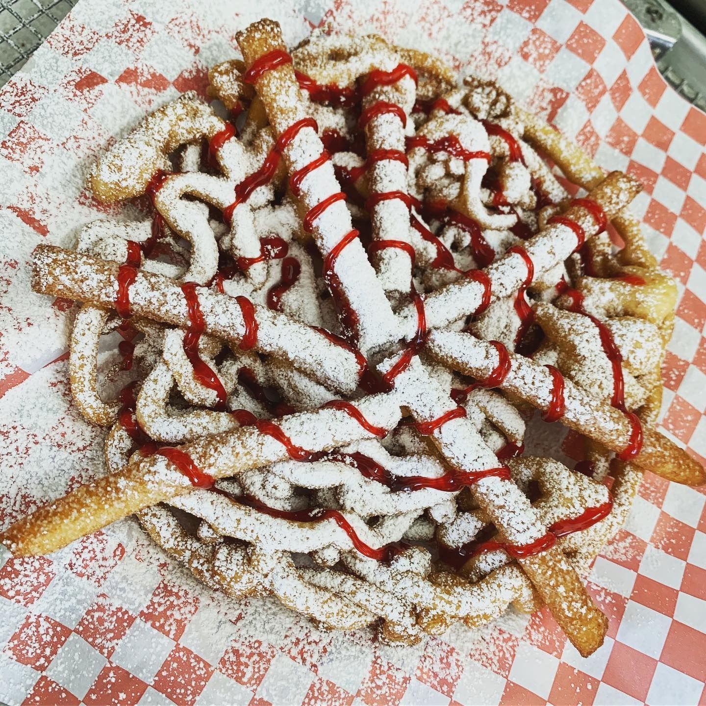 Fries topped with red sauce and white drizzle on red-and-white checkered paper.