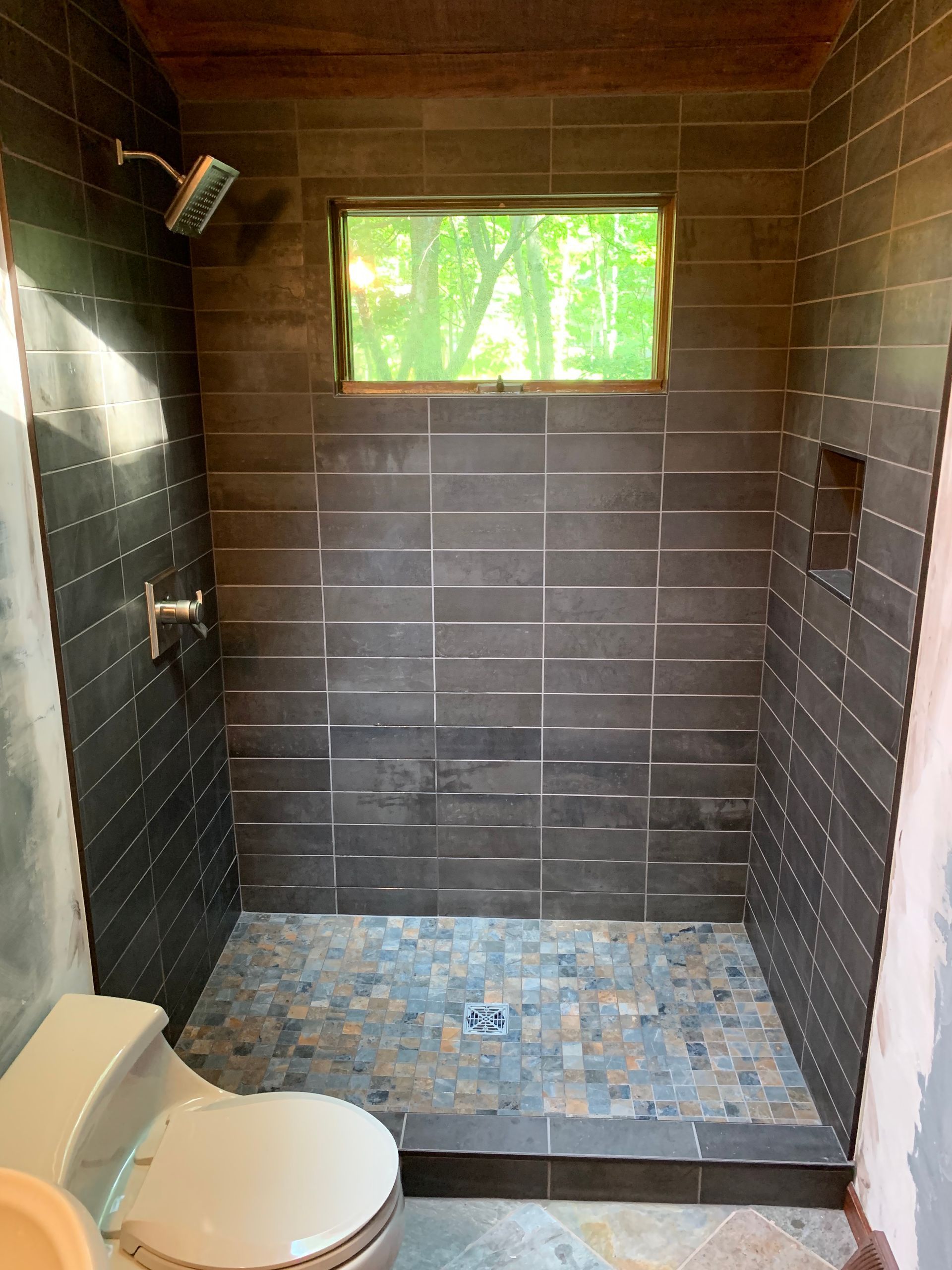 A bathroom with a toilet , sink , shower and window.
