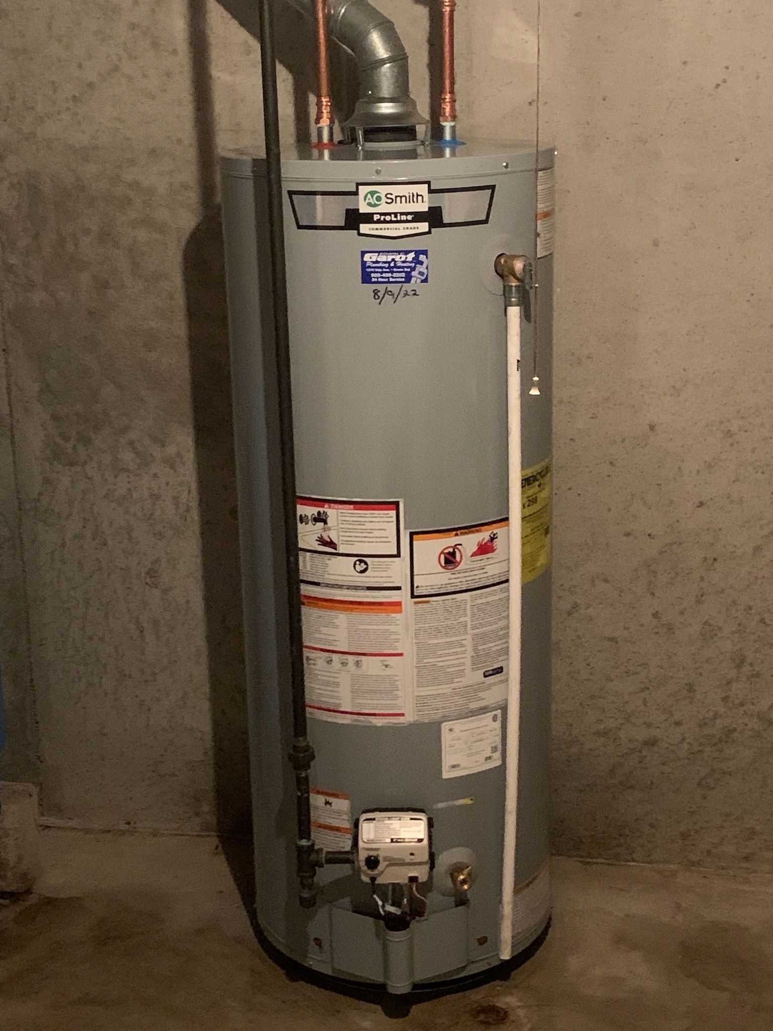 A water heater is sitting in a basement next to a wall