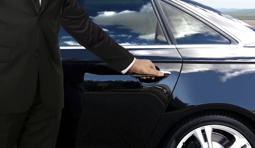 A man in a suit is opening the door of a black car.