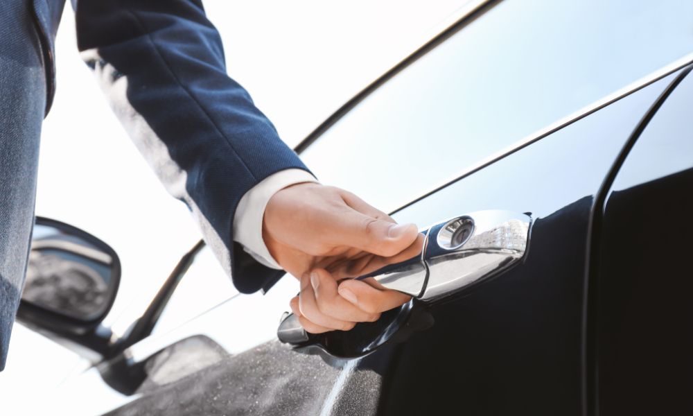 A man in a suit is opening the door of a black car.