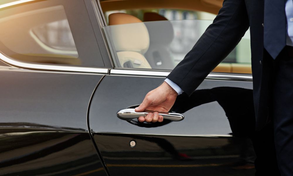 A man in a suit is opening the door of a black car.