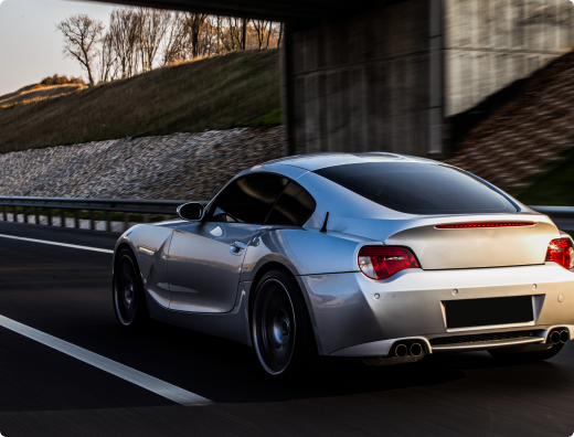 A silver sports car is driving down a highway under a bridge