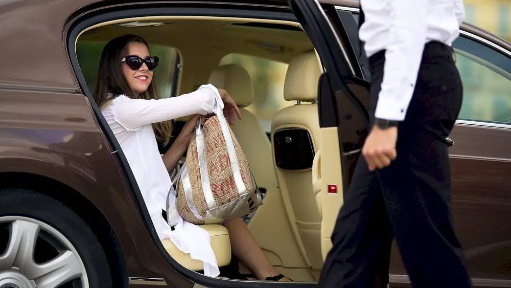 A woman is sitting in the back seat of a car while a man opens the door.