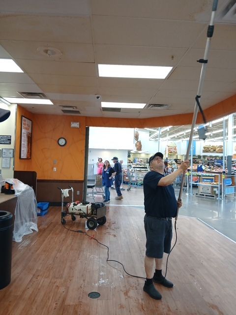Person scrubbing a tile floor with a brush and cleaning spray bottle nearby