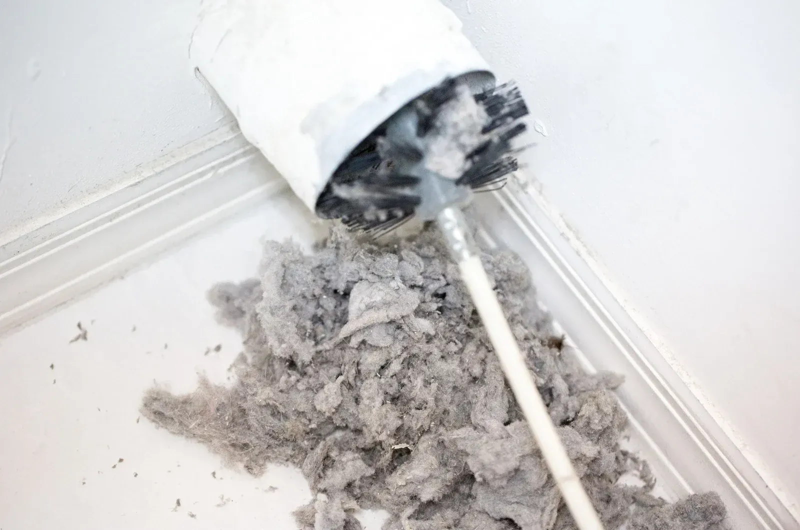 Dust and debris spilling from a white vacuum cleaner onto a white floor corner