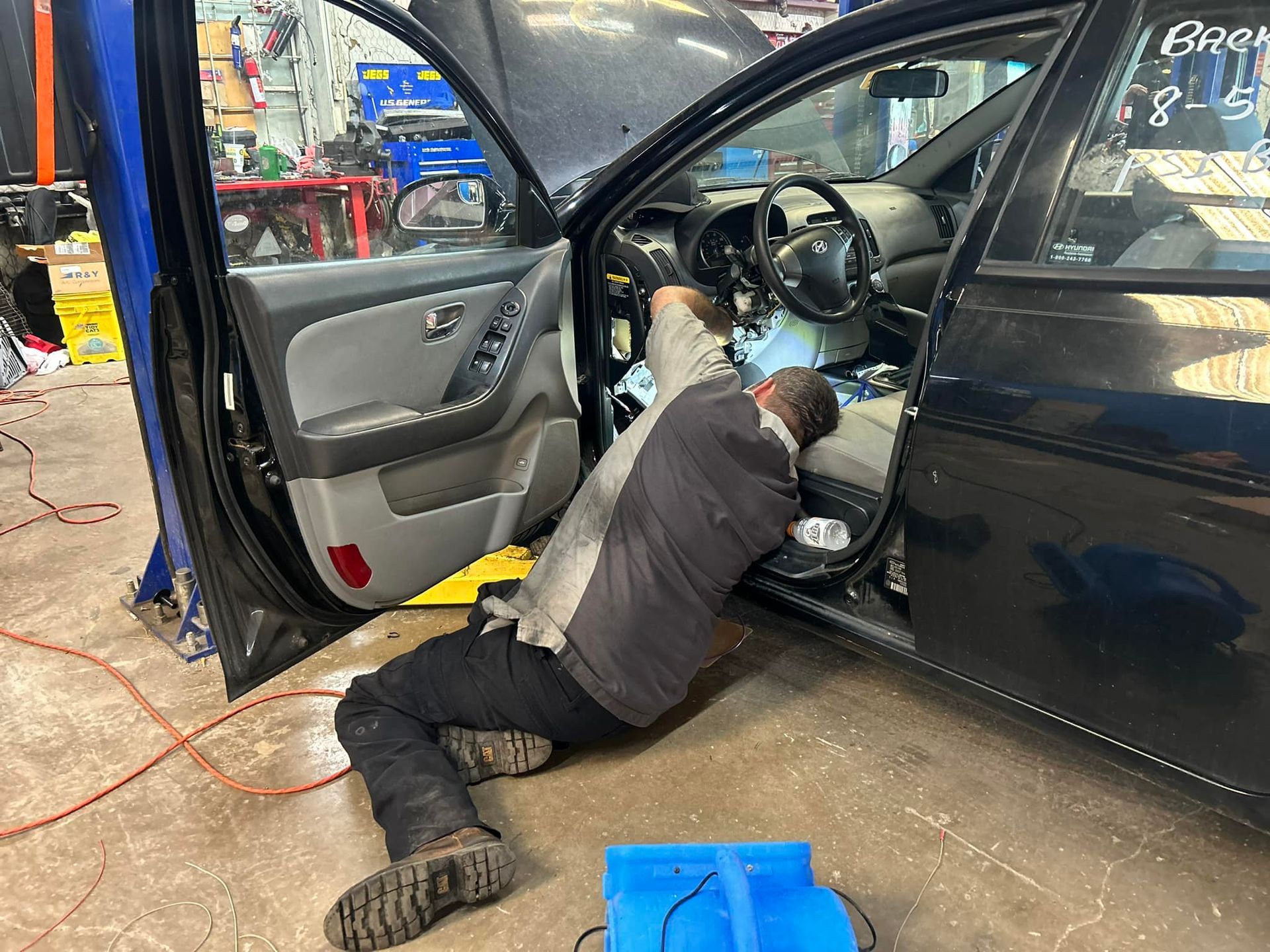 Mechanic working on the dashboard of a black car in a garage. Car door is open.
