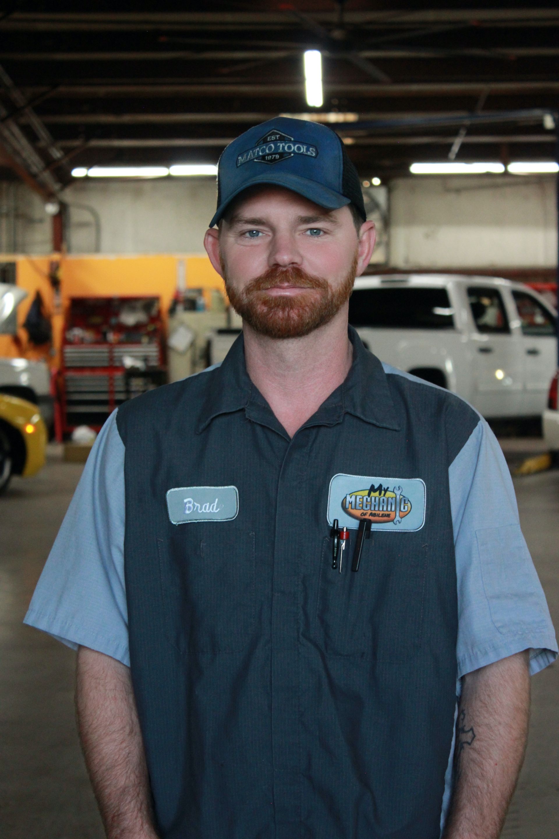 Mechanic in a blue uniform, standing in a garage, wearing a cap.