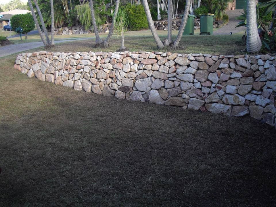A Large Stone Wall Is Surrounded By Grass And Trees — Australian Rock Walls In Bundaberg, QLD