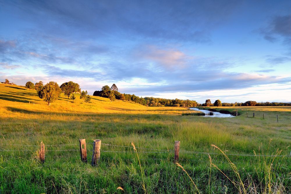 A Fence Surrounds A Grassy Field With A River In The Background — Australian Rock Walls In Cleveland, QLD