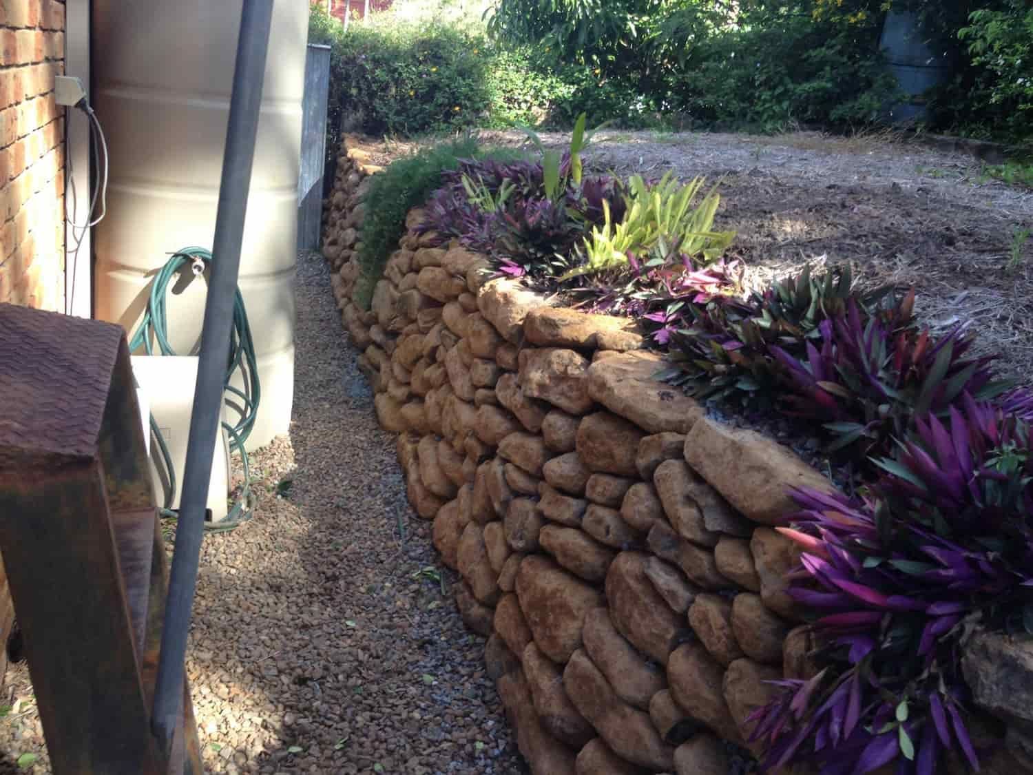 a Stone Wall Surrounds a Garden With Purple Flowers — Australian Rock Walls In Burleigh Heads, QLD