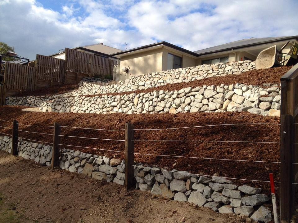 A Stone Wall With A Barbed Wire Fence In Front Of A House — Australian Rock Walls In Burleigh Heads, QLD