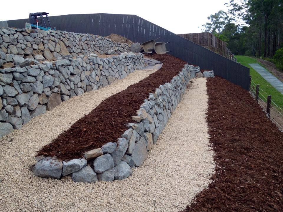 A Stone Wall With A Barbed Wire Fence In Front Of A House — Australian Rock Walls In Burleigh Heads, QLD