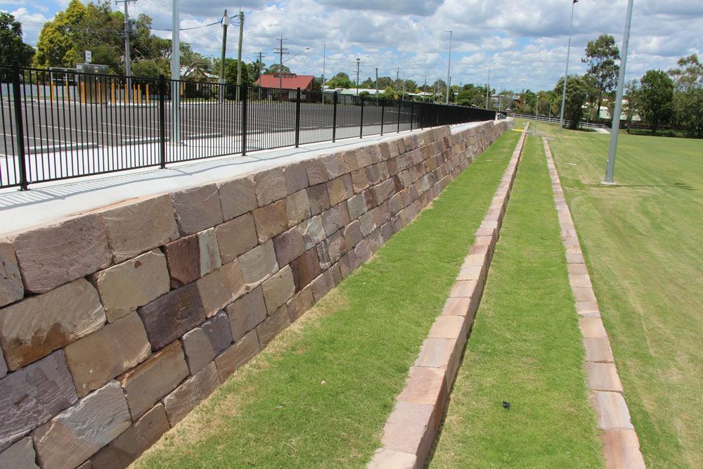 Sandstone block retaining wall on a Gold Coast property with safety railing along a grassed embankment