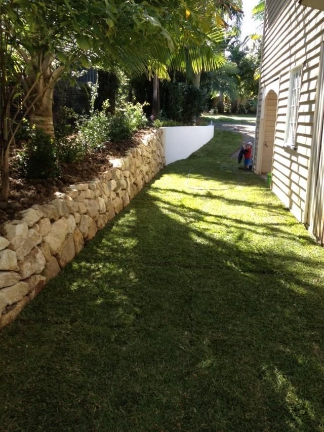 A Person Is Kneeling In The Grass Next To A Stone Wall — Australian Rock Walls In Gold Coast, QLD