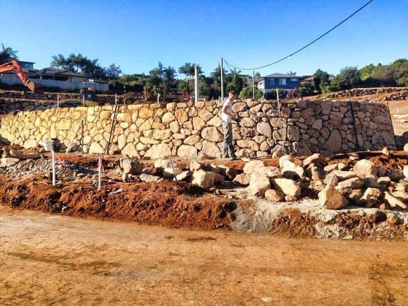 A Man is Working on a Stone Wall in a Dirt Field  — Australian Rock Walls In Burleigh Heads, QLD