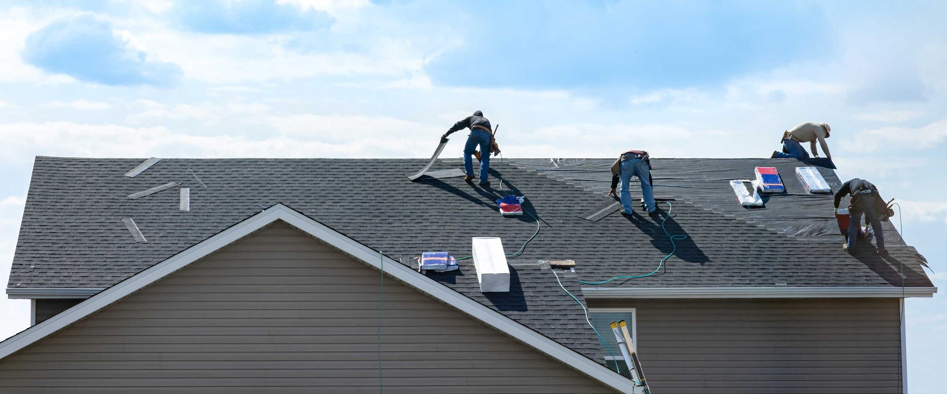Four men using tools and safety gear for maintenance work by a roofing repair contractor on a home.