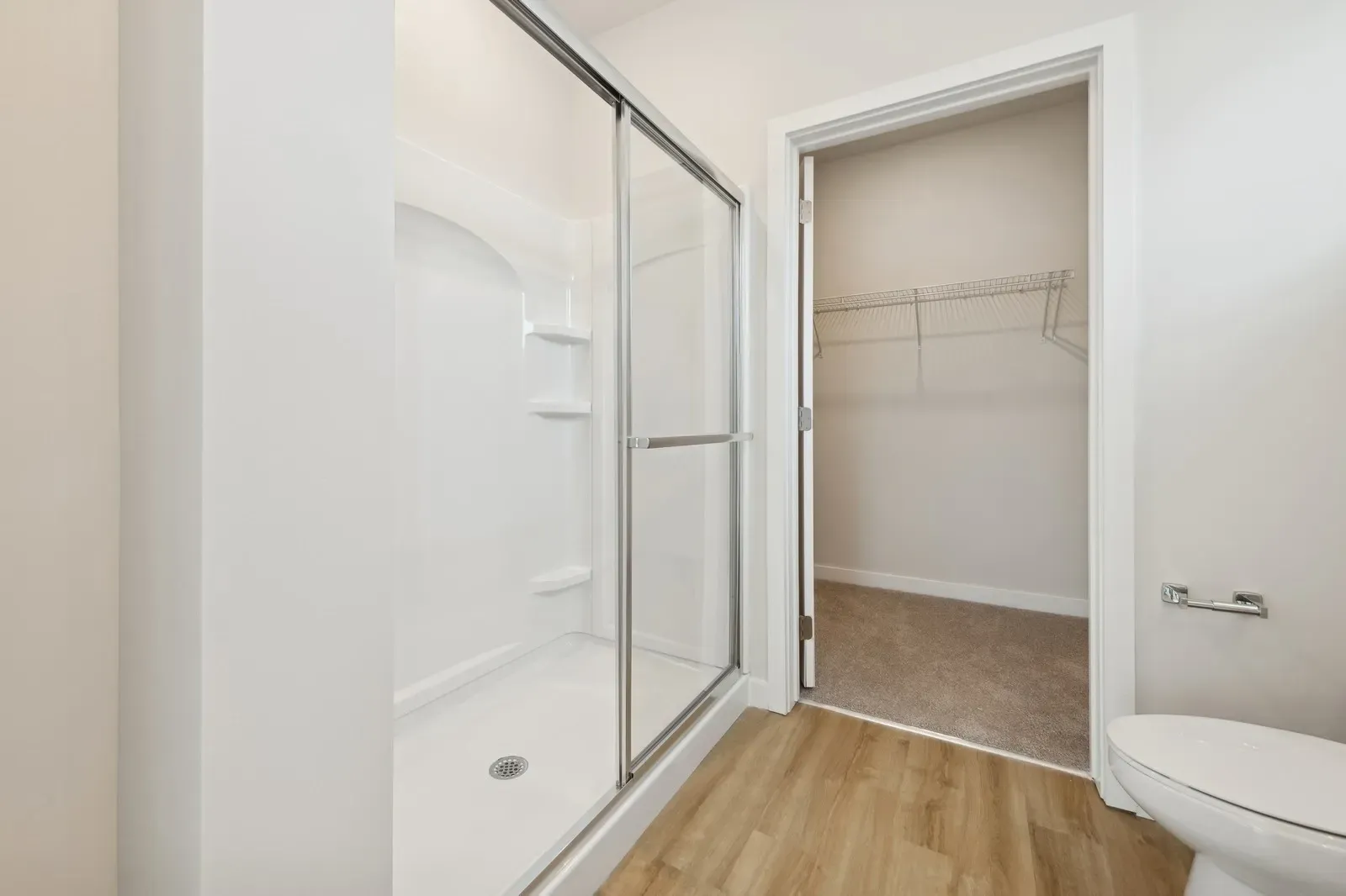 Bathroom with a glass sliding shower enclosure, wood-look flooring, and a walk-in closet.