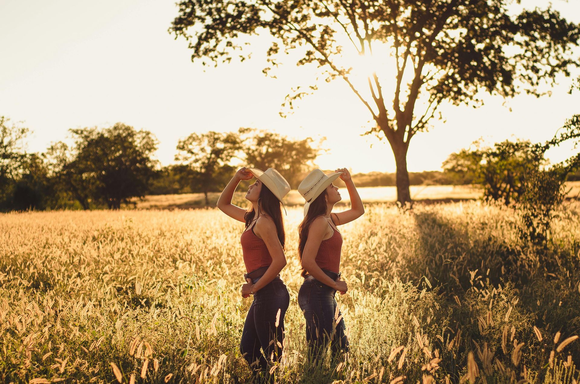 Two women wearing cowboy hats are standing in a field.
