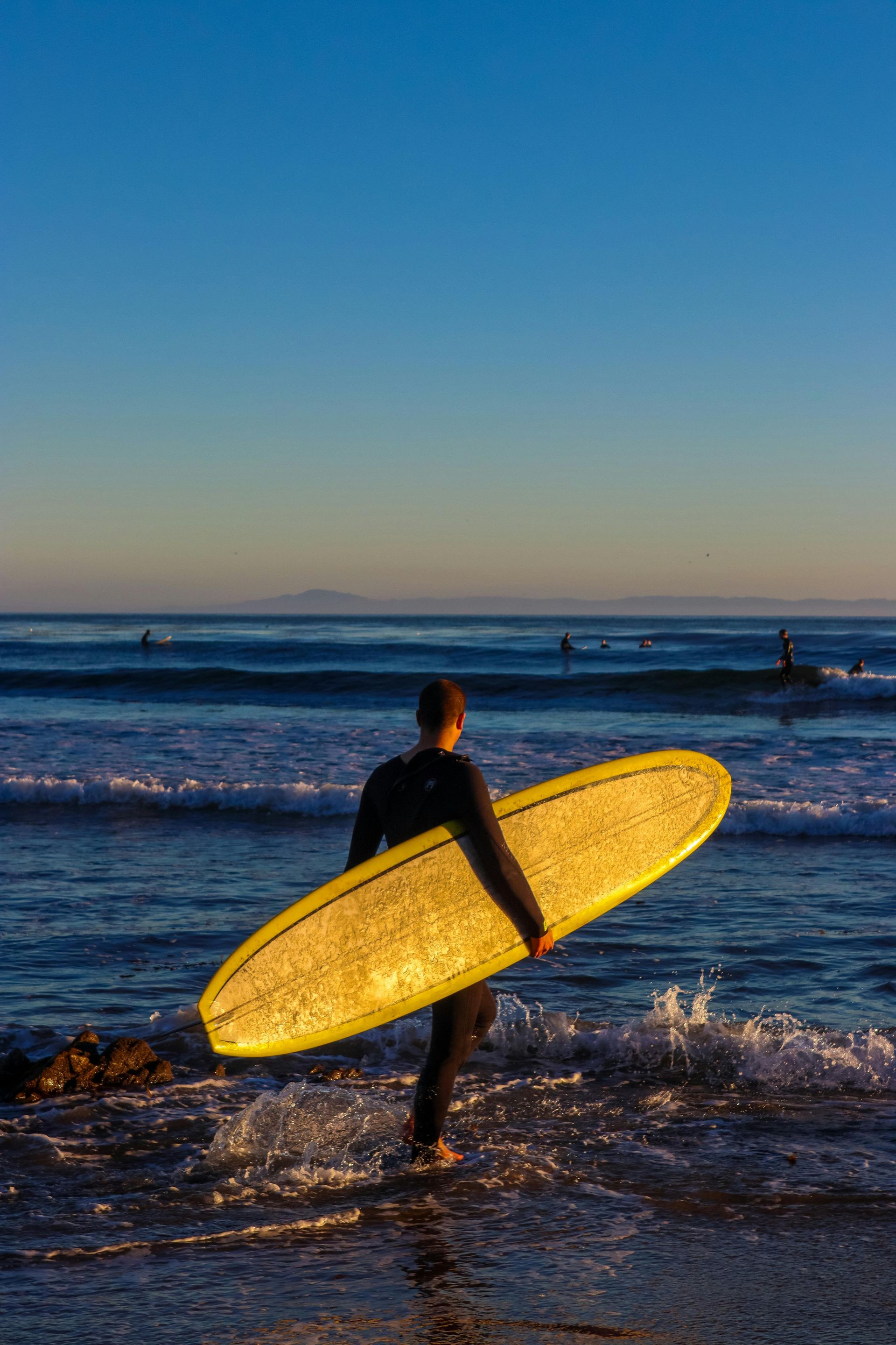 A man is carrying a surfboard into the ocean.