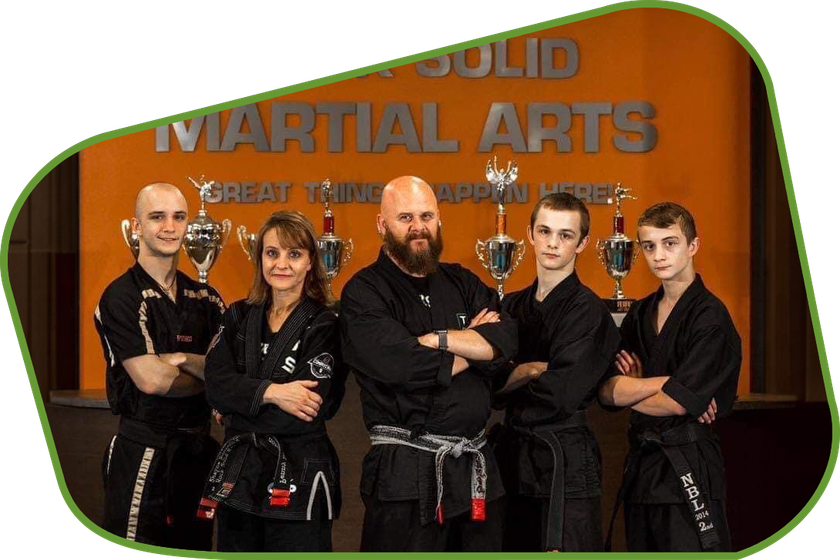 a group of martial arts students pose in front of a solid martial arts sign